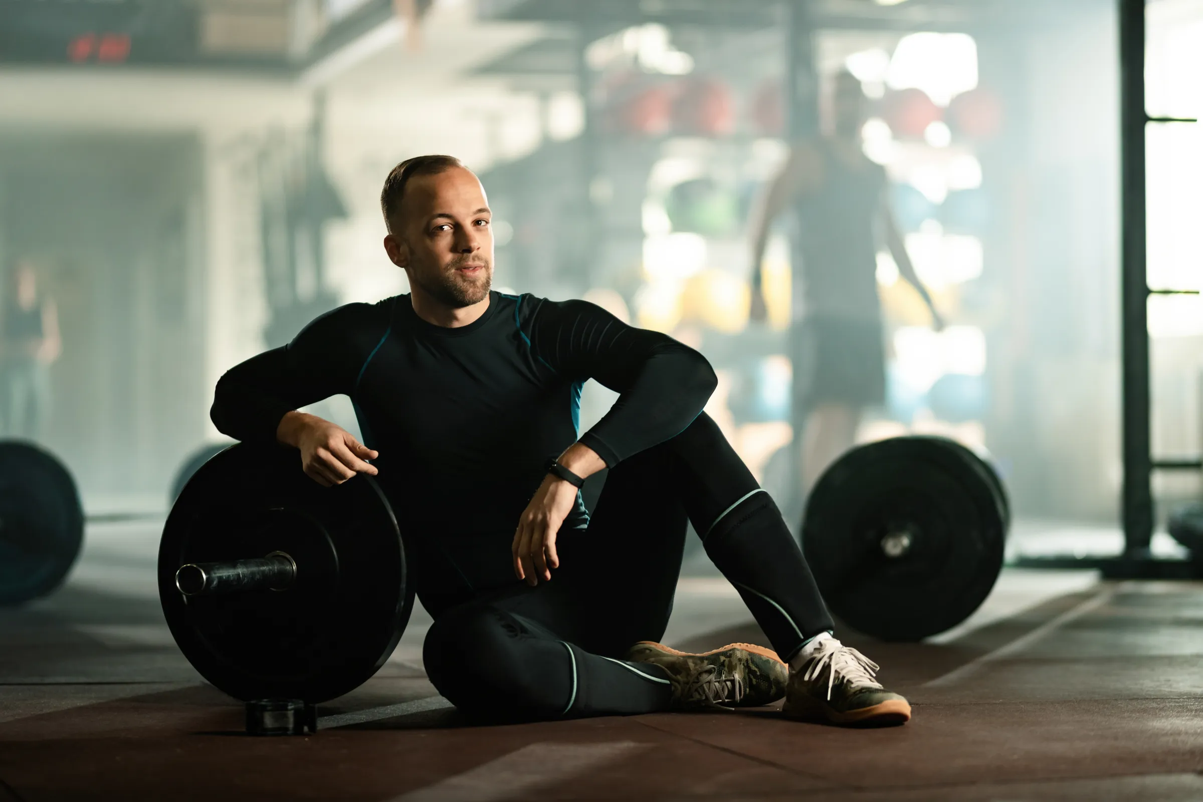 Hombre descansando sentado junto a los discos en un gimnasio